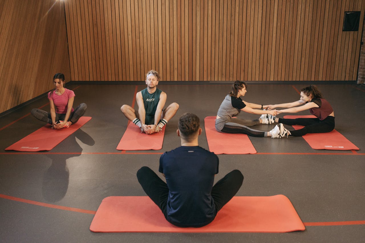 gallery-04 People engaging in a yoga class with red mats in an indoor wooden studio.