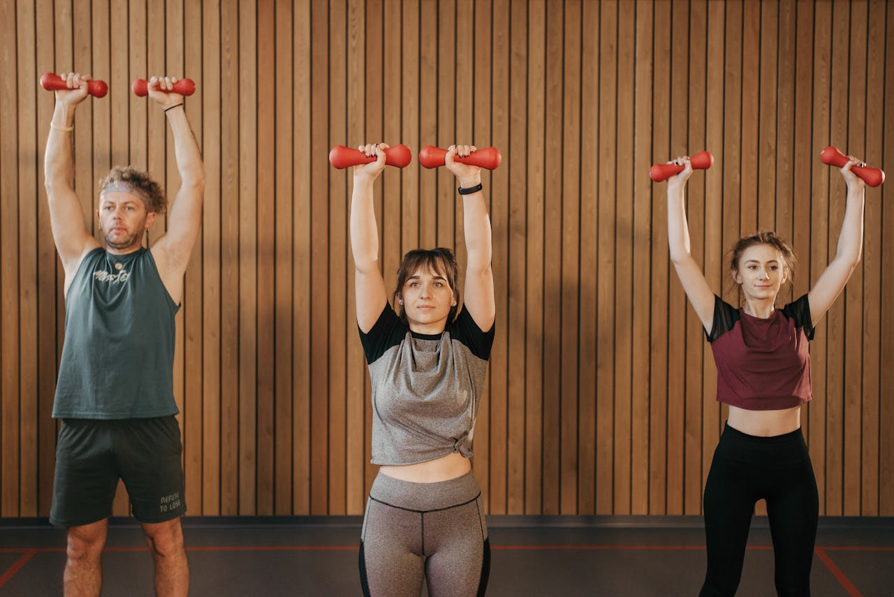 Three people exercise with dumbbells in an indoor fitness class, focusing on strength training.